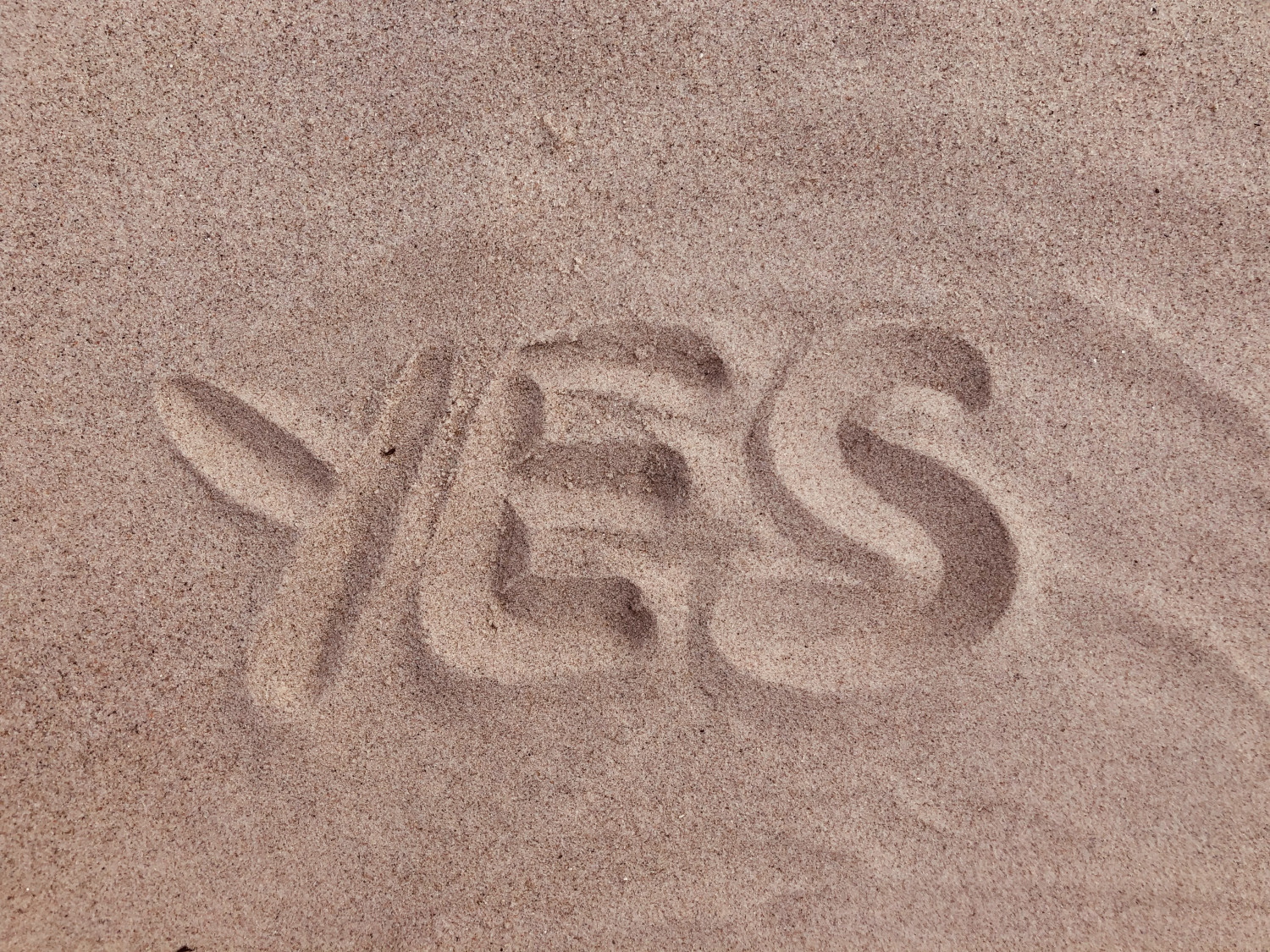 The word Yes written in sand