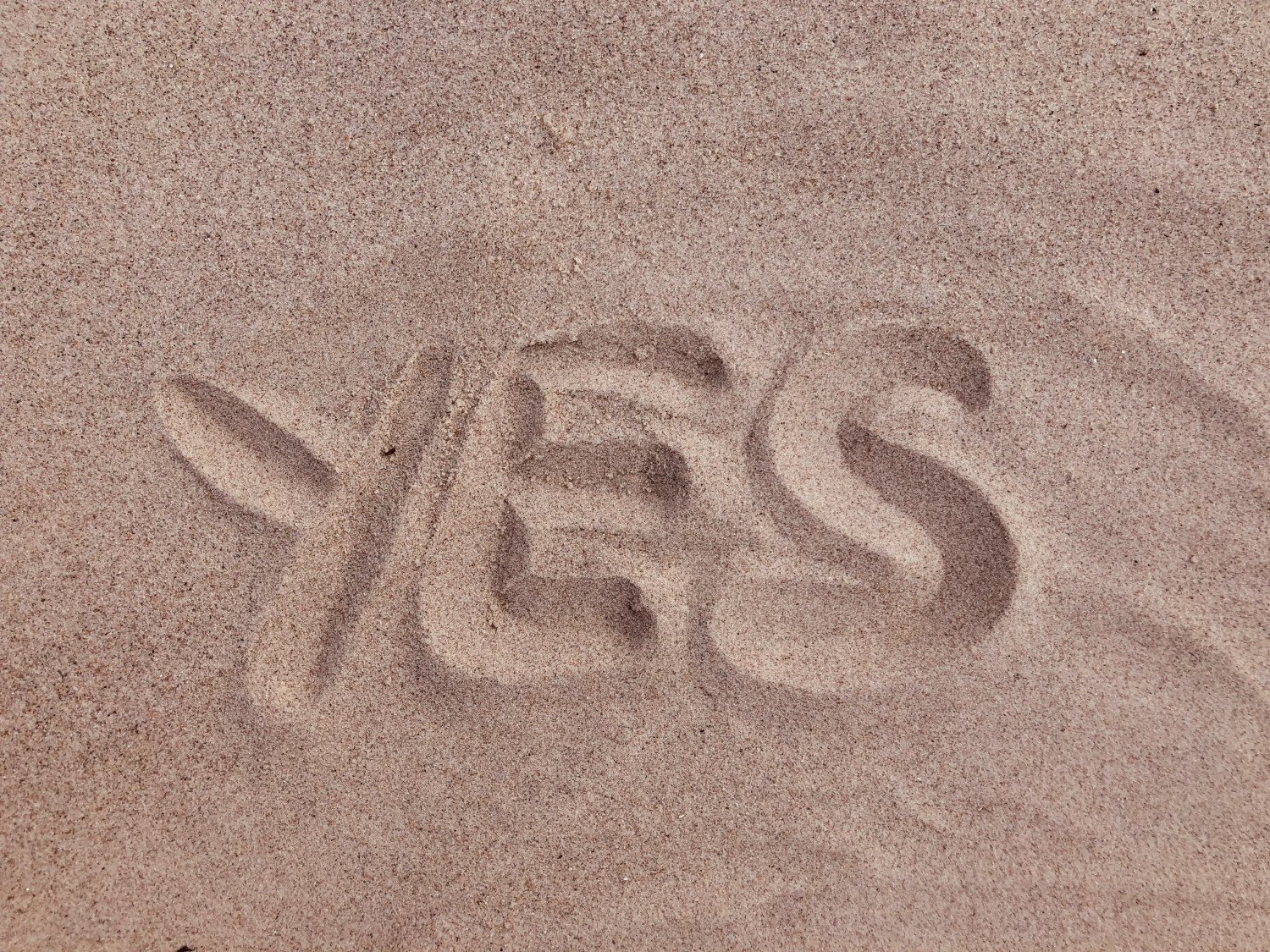 The word Yes written in sand
