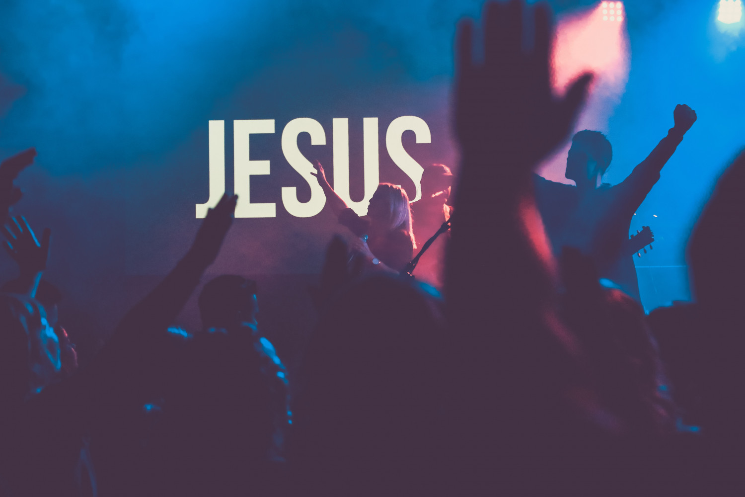 Image of people worshipping in front of a sign that says 'Jesus'